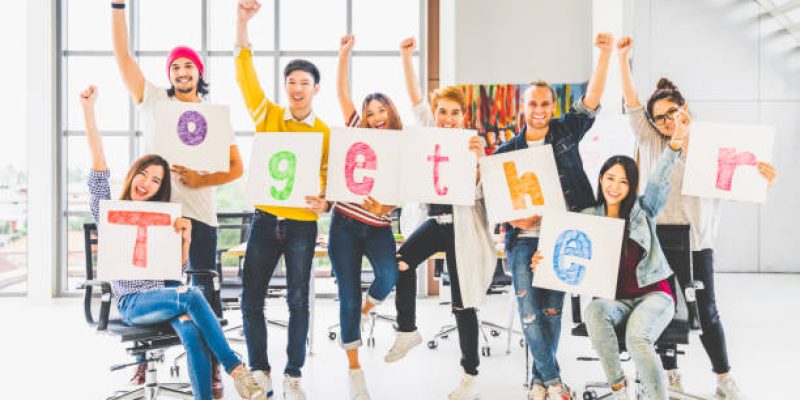 Multiethnic diverse group of office coworkers or creative team cheering and celebrating, holding letter banner papers written together word. Colleague partner teamwork, team building, empowerment, or friendship togetherness concept